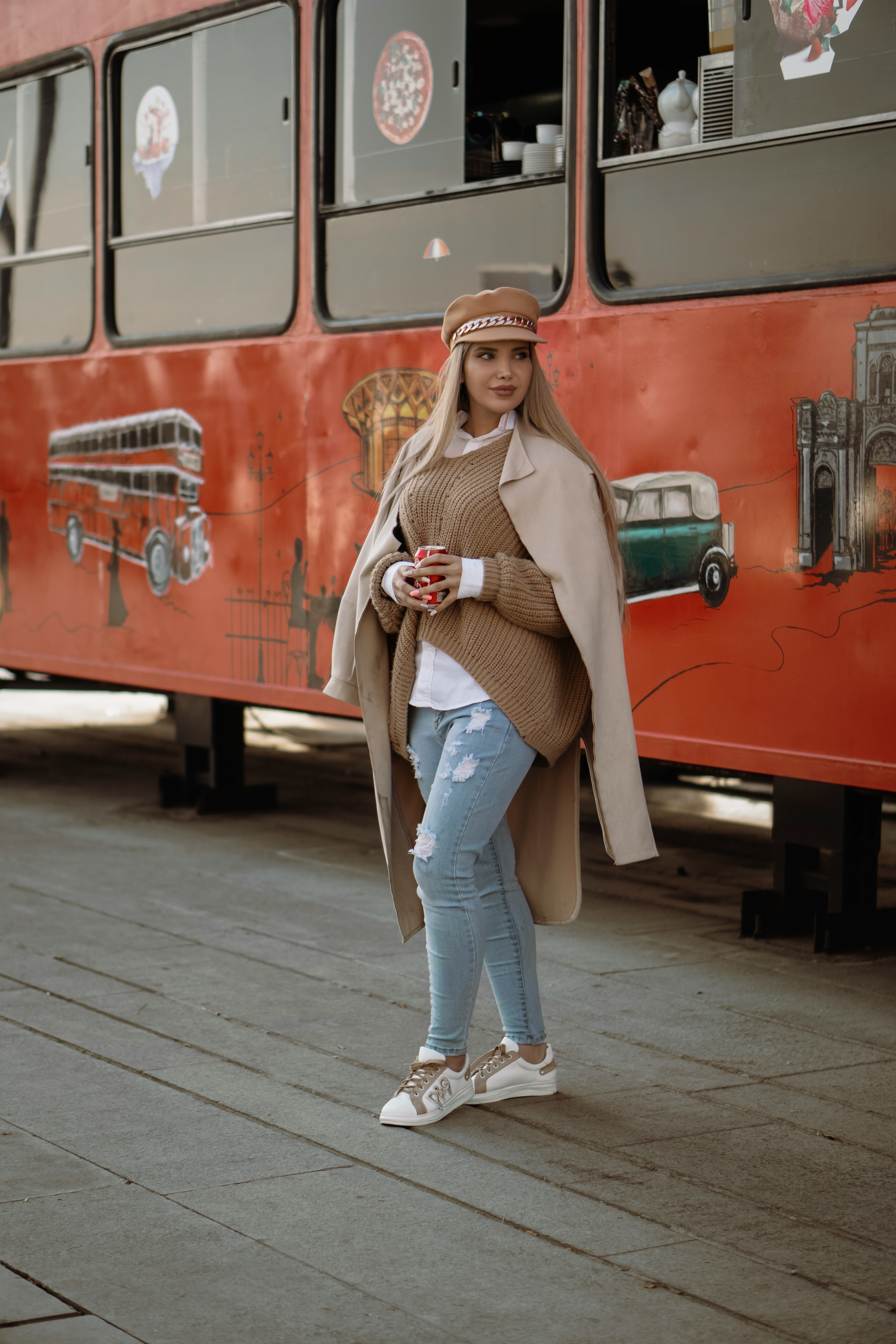 woman in brown coat and blue denim jeans standing beside red bus